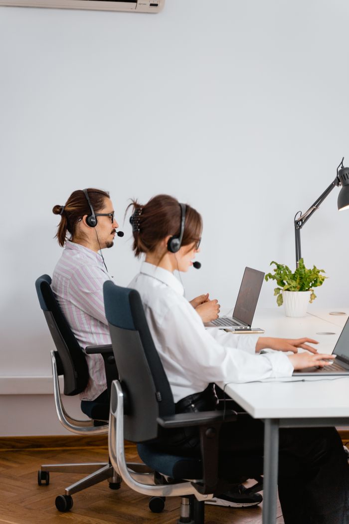 Services-01 Two call center employees working with laptops and headsets in an office.